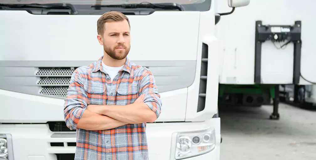 A man standing with his arms crossed in front of an 18-wheeler.