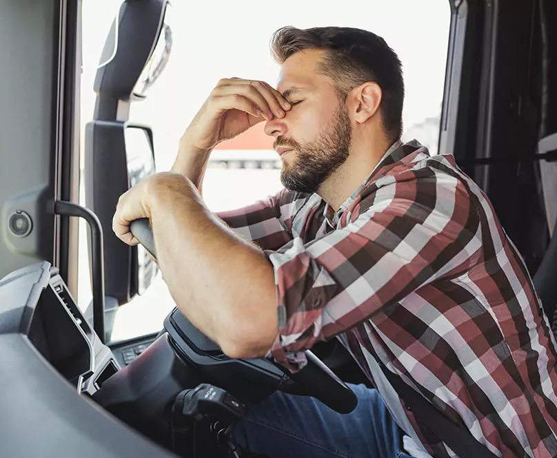 A man holding his hand to his face inside of an 18-wheeler.